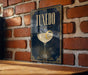 A framed poster of a cocktail glass with a lemon peel, mounted on a brick wall.