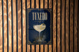 A framed poster with the word "Tuxedo" on it, featuring an illustration of a martini glass with a lemon twist.