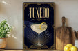 A framed poster of a cocktail glass with a lemon on top, placed on a shelf next to a wooden cutting board and some lemons.