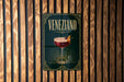 A sign for Veneziano cocktail is displayed on a wooden wall.
