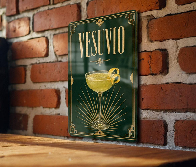 A framed poster of a cocktail glass with a yellow drink inside, hanging on a brick wall.