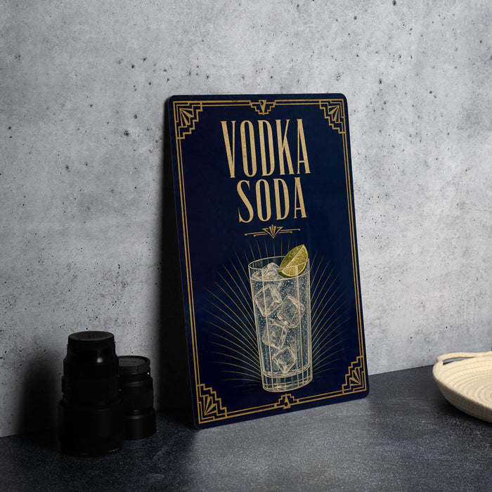 A blue sign with gold lettering and an illustration of a glass of vodka soda, placed on a gray countertop next to a stack of black containers.