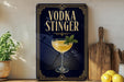 a decorative sign with the text "VODKA STINGER" and an illustration of a cocktail glass with a mint garnish.