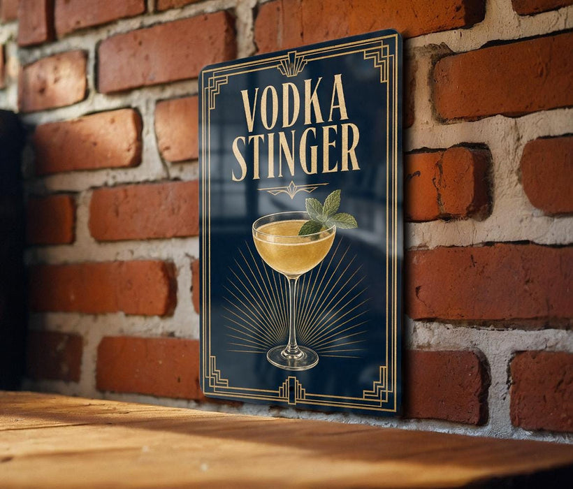 A sign with the text "VODKA STINGER" and an illustration of a cocktail glass with a mint garnish, mounted on a brick wall.
