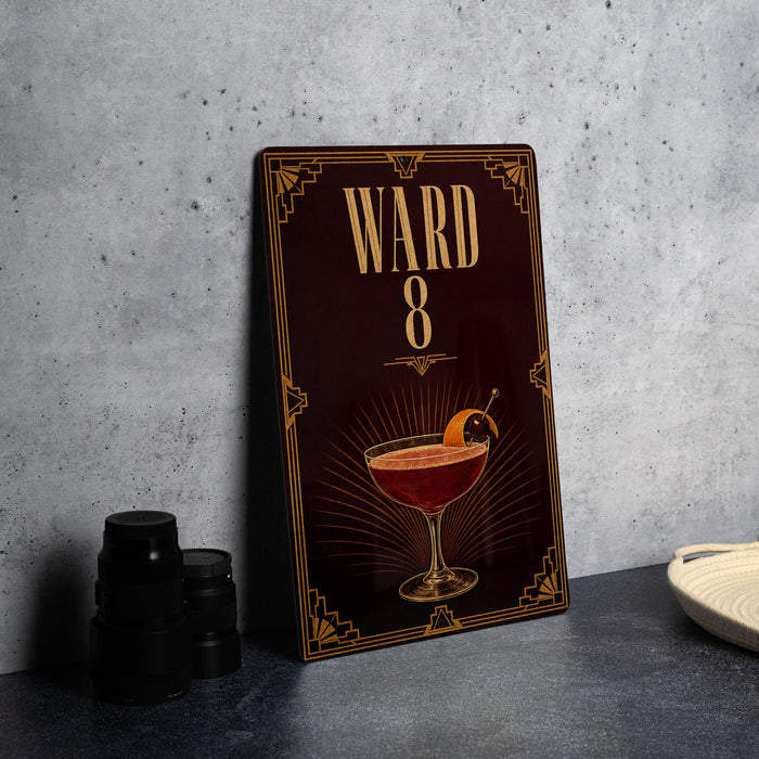 A dark wooden sign with a decorative border and a large illustration of a cocktail on it, placed on a gray countertop next to some black camera lenses.