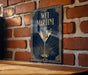 A framed poster of a martini glass with a green olive on a brick wall.
