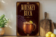 A copper mug filled with a drink, accompanied by a lemon slice, is featured prominently on a wall-mounted sign that reads "Whiskey Buck".