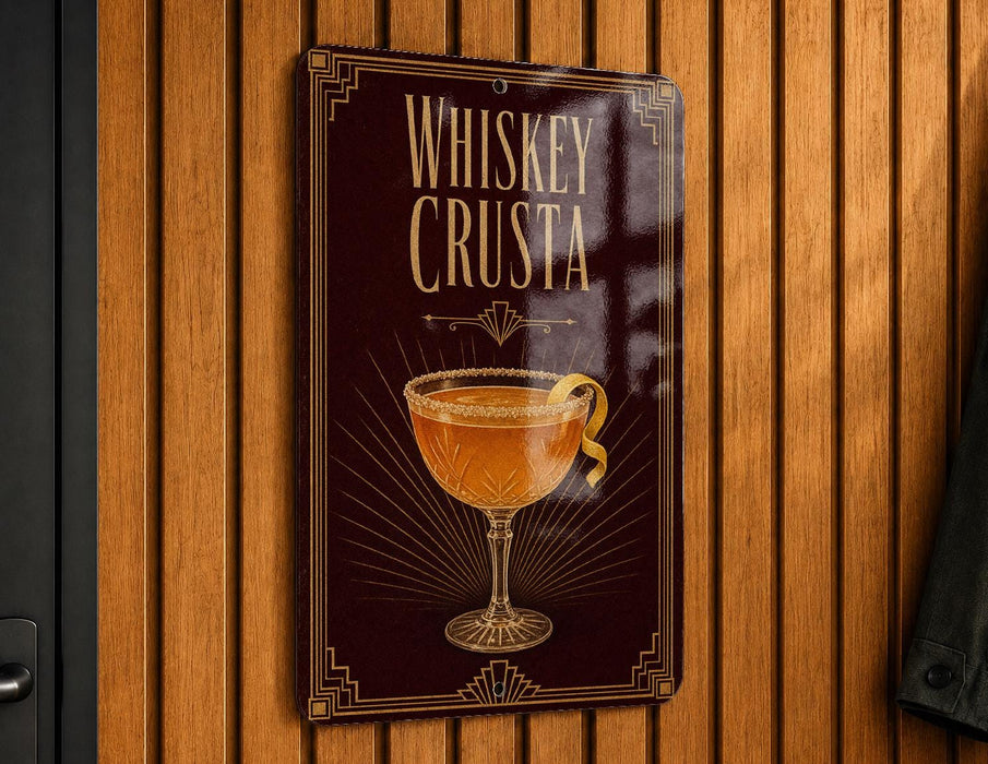 A metallic sign with a decorative design hangs on a wooden wall, featuring an illustration of a whiskey crusted cocktail.