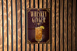 A sign for whiskey ginger cocktail is displayed on a wooden wall.