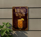 A metallic sign with the text "Whiskey Ginger" and an illustration of a cocktail is displayed on a wall, with a plant visible to the left.