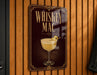 A metallic sign with the text "Whiskey Mac" and an illustration of a cocktail glass with a lemon twist.