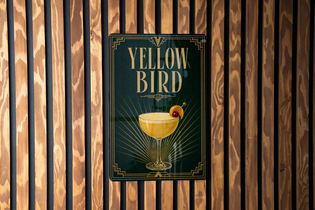 A sign for a cocktail called "Yellow Bird" is displayed on a wooden wall.