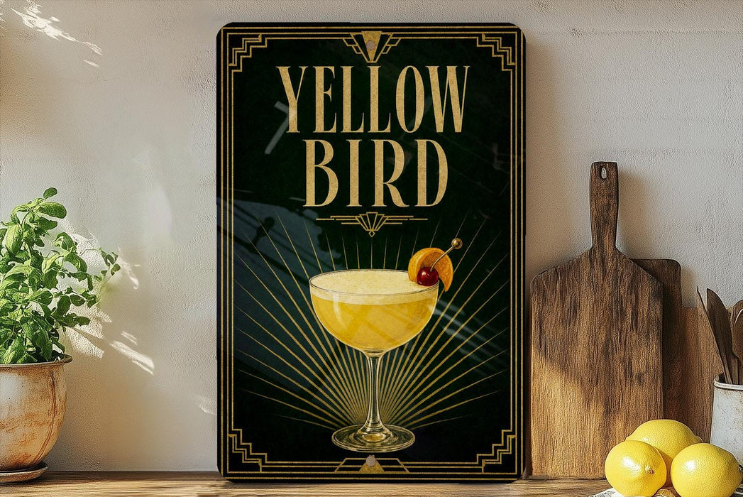 A framed poster with the text "YELLOW BIRD" and an illustration of a cocktail glass with a lemon slice on top, placed on a wooden shelf next to a wooden cutting board and a potted plant.