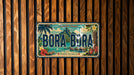 A vintage license plate with the text "BORA BORA" and tropical imagery, mounted on a wooden wall.