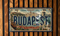 A vintage-style license plate from Hungary with the word "BUDAPEST" prominently displayed, featuring an illustration of the city of Budapest.