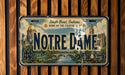 A vintage license plate from Notre Dame, Indiana, with a design depicting the Notre Dame Cathedral and surrounding landscape.