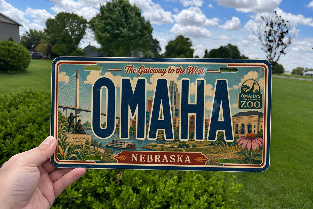 A person is holding a license plate from Nebraska that says "OMAHA NEBRASKA" with a scenic illustration of the state's landmarks and natural beauty.