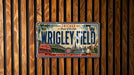 A vintage Chicago Cubs baseball plate with the text "Chicago Home of the Cubs" and "Wrigley Field" printed on it, mounted on a wooden wall.