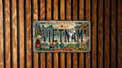 A vintage license plate from Vietnam, featuring an illustration of the country's landscape and culture, is displayed on a wooden wall.