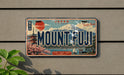 A vintage Japanese license plate with the text "MOUNT FUJI" prominently displayed, along with various scenic elements such as a temple, cherry blossom trees, and a mountain.