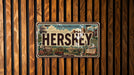 A vintage-style license plate with the word "HERSHEY" prominently displayed, mounted on a wooden wall.