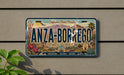 A license plate with the text "ANZA-BORREGO" and "California's Desert Paradise" printed on it, along with illustrations of desert landscapes and landmarks.