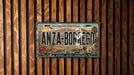 A vintage California license plate with the text "ANZA-BORREGO" and a desert landscape illustration, mounted on a wooden wall.
