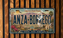 A vintage license plate with the text "ANZA-BORREGO" and various desert-themed illustrations, including mountains, cacti, and a bird.