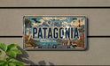 A vintage Patagonia license plate with a scenic mountain landscape and a lighthouse, mounted on a wall.