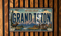 A vintage license plate from Grand Teton National Park, featuring a scenic mountain landscape with a moose and cabin in the foreground.