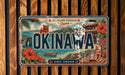 The image is a vintage license plate from Japan that features a tropical island landscape with a temple, flowers, and a lion.
