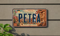 A vintage-style license plate with the word "PETRA" prominently displayed, featuring an illustration of a desert landscape with a building and mountains in the background.
