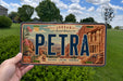 A person is holding a license plate with the word "PETRA" on it, which is located in Jordan.