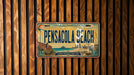 A vintage license plate from Pensacola Beach, Florida, with a beach scene and ocean in the background.