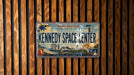 A vintage Florida license plate with the text "Florida's Space Coast" and "KENNEDY SPACE CENTER" printed on it, mounted on a wooden wall.