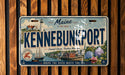 A license plate from Maine, with a vintage design featuring a lighthouse, boats, and a coastal town.