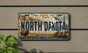 A vintage license plate from North Dakota, featuring an illustration of a buffalo, mountains, and a city skyline.