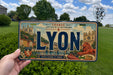 A person is holding a license plate with the word "LYON" prominently displayed on it.