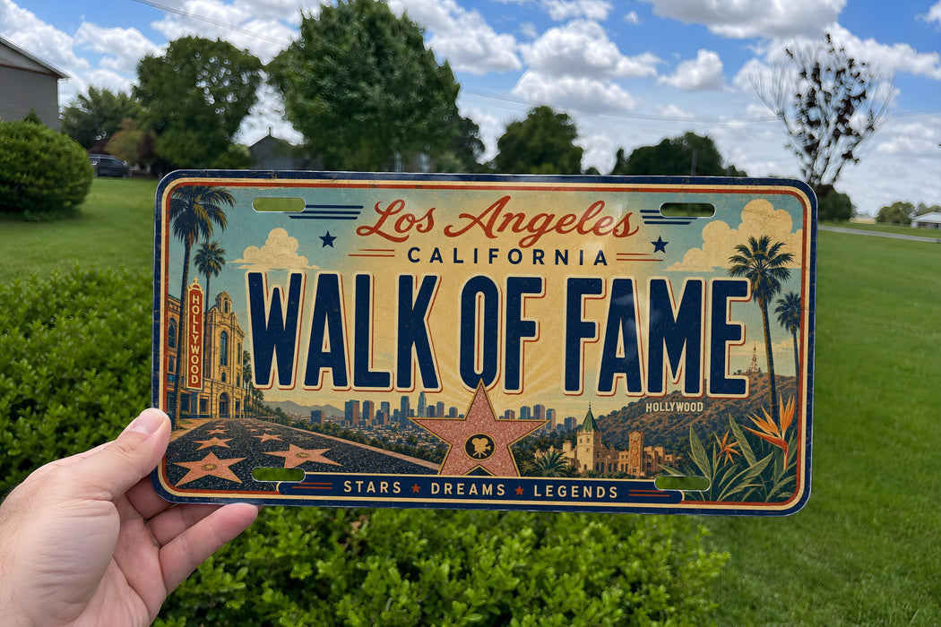 A person is holding a California license plate with the text "WALK OF FAME" on it, against a background of a grassy field and trees.