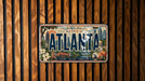 A decorative license plate from Georgia, featuring the city's skyline and landmarks, is displayed on a wooden wall.