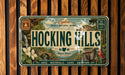 The image is a vintage license plate with a nature-themed design, featuring a waterfall, a bridge, and various outdoor elements.