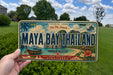 A vintage-style license plate from Thailand, featuring the text "MAYA BAY THAILAND" and a scenic illustration of the island.