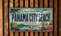A vintage license plate from Panama City Beach, Florida, featuring a beach scene with palm trees, a pier, and a city skyline.