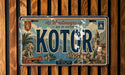 A vintage license plate from the town of Kotor, located in the Bay of Kotor, with a scenic illustration of the town and surrounding mountains.