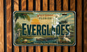 A license plate with a tropical landscape featuring palm trees, a sunset, and various wildlife, including a heron and a crocodile.