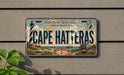 A license plate with the text "Cape Hatteras" and a lighthouse image, mounted on a wall.