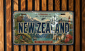 A vintage license plate from New Zealand, featuring a scenic landscape with mountains, a lighthouse, and a small boat.