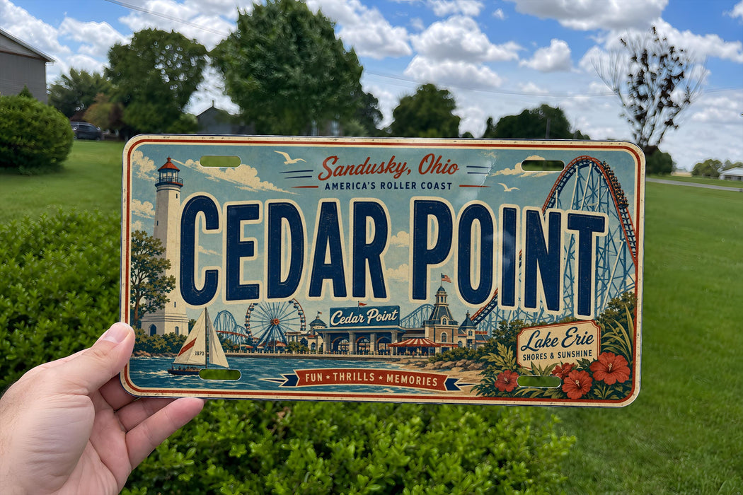 A person is holding a license plate that features an illustration of Cedar Point, an amusement park located in Sandusky, Ohio.