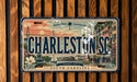 A license plate from Charleston, South Carolina, featuring a vintage design with a cityscape, palm trees, and a horse-drawn carriage.