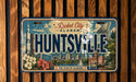 A vintage license plate from Alabama that reads "HUNTSVILLE" with a cityscape and rocket launch in the background.